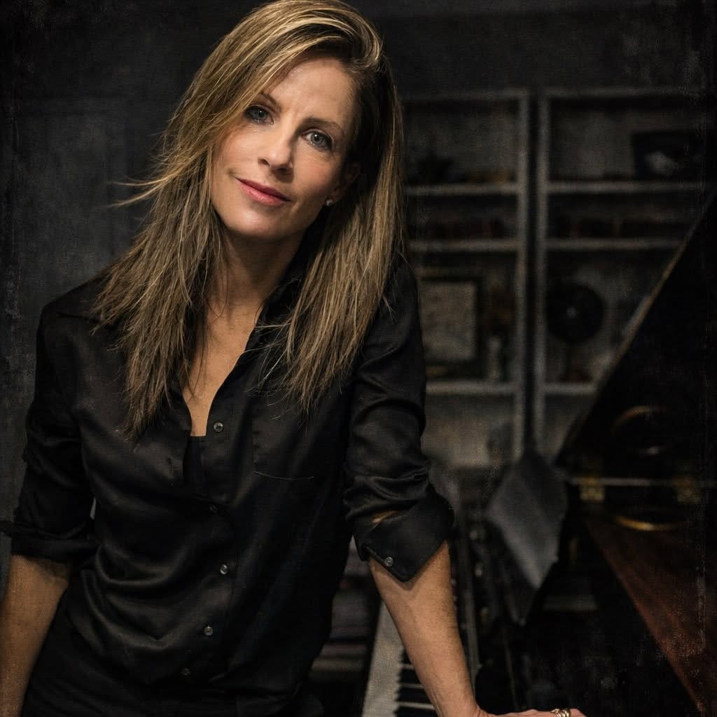 Rachelle Risling leaning on a piano in a dark studio